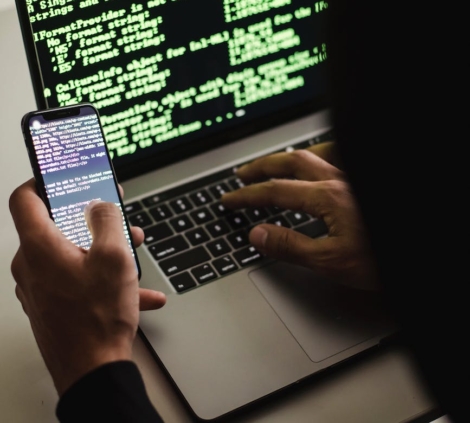 unrecognizable hacker with smartphone typing on laptop at desk
